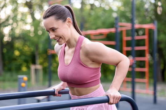 Athletic woman exercising on parallel bars at outdoor gym