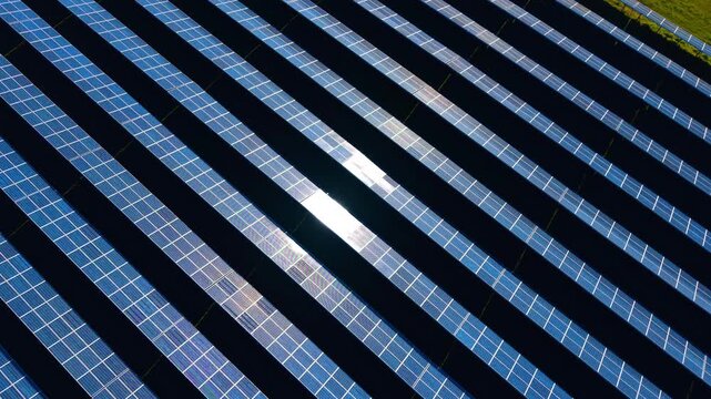 Abstract aerial view of solar panel rows with sun reflection. Factual top down drone photograph of parallel blue photovoltaic solar modules reflecting bright sunlight glare.