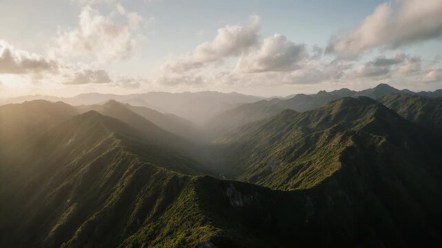 Sunlit mountain ridges stretching into misty distance beneath soft clouds in panoramic natural landscape
