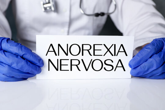 Doctor holding card with words Anorexia Nervosa at table, closeup
