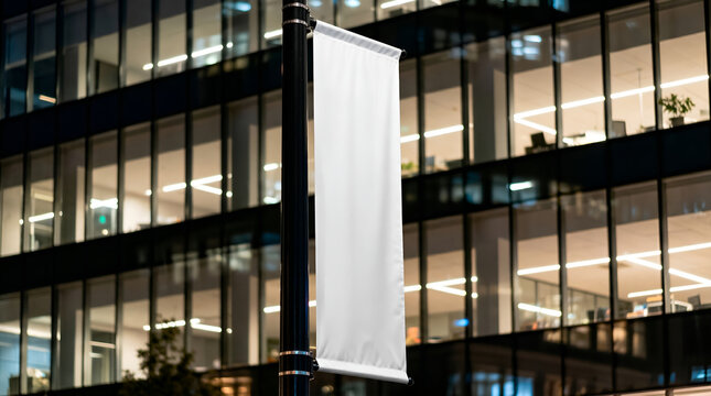 Blank white banner mockup hanging on a pole in front of a modern office building at night