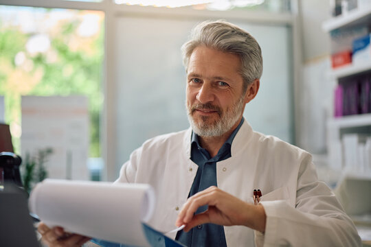 Smiling mature pharmacist at work looking at camera.