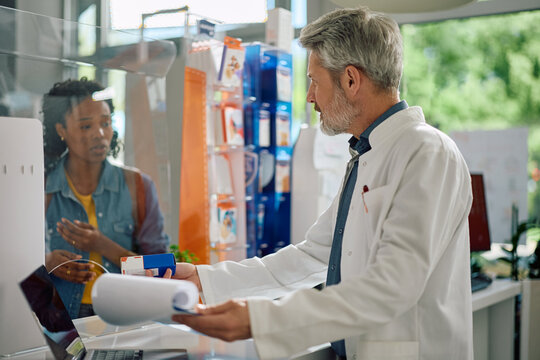 Mature pharmacist giving prescription medicine to customer in pharmacy.