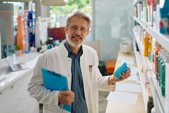Happy mature pharmacist working in drugstore and looking at camera.
