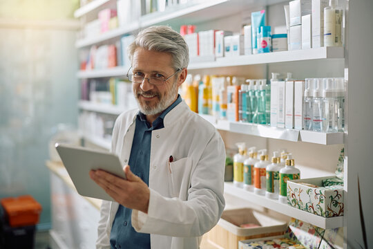 Happy pharmacist working on touchpad and looking at camera.