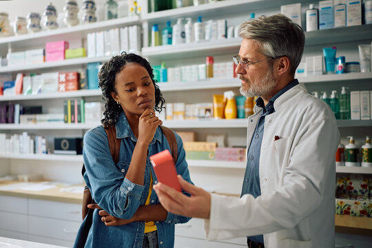 Black woman consulting with her pharmacist while looking for skincare product in drugstore.