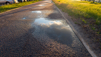 Damp asphalt trail reflecting the sky and clouds in a puddle during the golden hour. Tranquil nature setting following a light rain shower © Bonsales