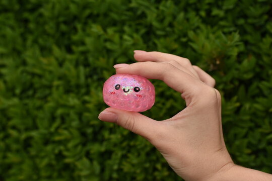 Horizontal photo of a hand holding a trendy dumpling squishy toy against a green natural background. Soft stress relief texture, summer atmosphere, natural lighting.