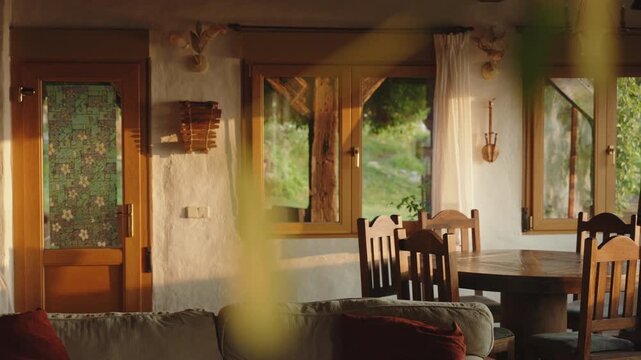 Sun-drenched dining area during golden hour, where warm light streams through wooden-framed windows to illuminate a rustic circular table, creating a serene, inviting space that bridges the comfort of