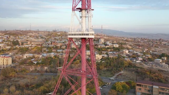 An aerial drone view of the Yerevan TV Tower standing tall over the misty Armenian capital during autumn with colorful forest and scenic city panorama in the background.

