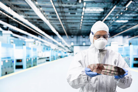 Analyzing processed silicon wafer, cleanroom and man in automated fabrication plant, Examining microelectronics for defects, semiconductor substrates and specialist doing quality control.