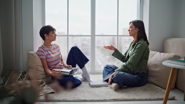 Cheerful besties sharing thoughts after reading sitting floor. Two women talking