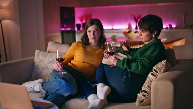 Friends enjoy girly evening sitting cozy home couch holding wine glasses. 