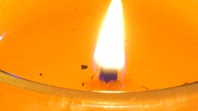 Burning candle wick flame in melted orange liquid wax close up