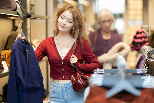 Young European woman holds a stylish dark blue coat in a clothing store. Shopping for outerwear in the shopping center