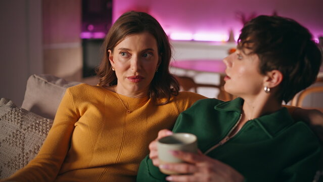 Women discussing TV show sitting home couch together closeup. Two girls talking 