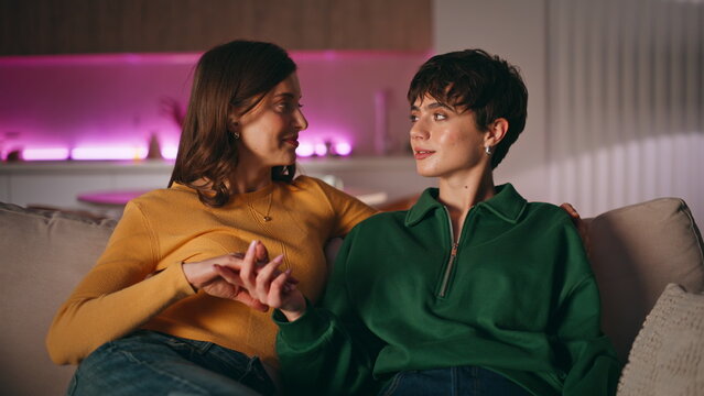 Lgbtq partners holding hands sitting couch looking each other with love closeup.