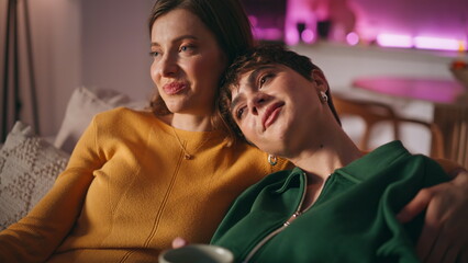 Fototapeta premium Tender couple watching film hugging on cozy home couch closeup. Lesbian partners