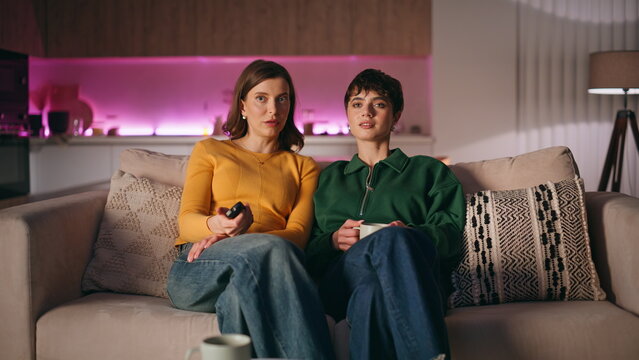 Girlfriends switching TV channels looking interesting show relaxing home couch.
