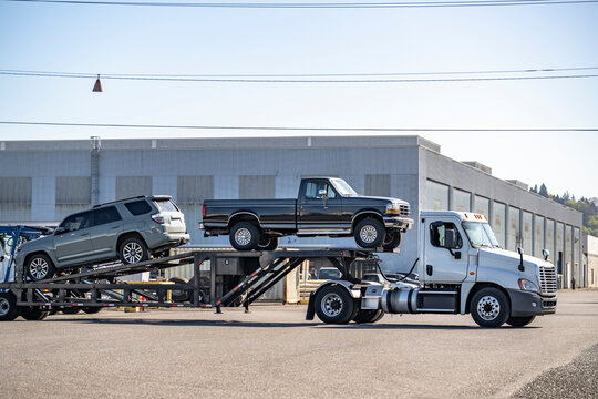 Big rig powerful day cab car hauler semi truck transporting cars on modular semi truck driving on the industrial warehouse parking lot