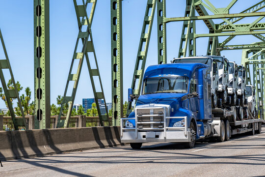 Bonnet blue big rig semi truck transporting cab over semi trucks on the step deck semi trailer running on the truss bridge