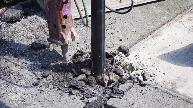Pneumatic drill breaking concrete pavement at road repair site with dust