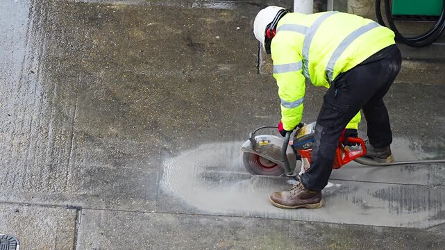Construction worker cutting concrete pavement with circular saw at road site