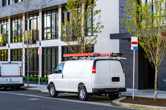 Cargo mini van with red ladder on the roof standing on the urban city street with modern multilevel apartments