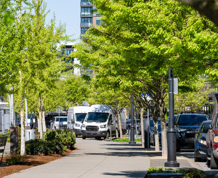 Compact white cargo mini vans standing on the green city alley making delivery to multilevel apartment