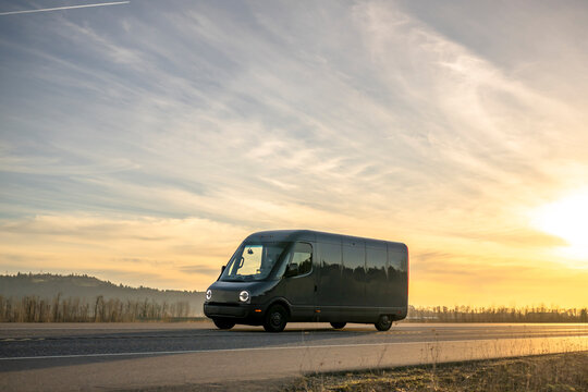 Dark gray electrical cargo mini van making delivery going on the road at sunset time