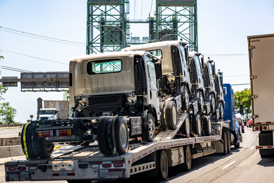 Powerful blue big rig semi truck transporting cab over semi truck tractors on step deck semi trailer running on the drawbridge
