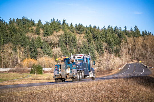 Powerful towing semi truck with lifting beam running on the winding road with winter forest on the hills