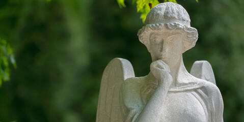 Obraz premium Thoughtful guardian angel statue in peaceful green surroundings. Copy space for text or design.