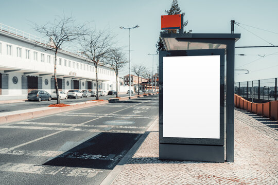 Large blank poster frame on modern bus stop beside quiet city road, offering clean outdoor advertising template space for poster design and transit branding; with a copy-space area on the left