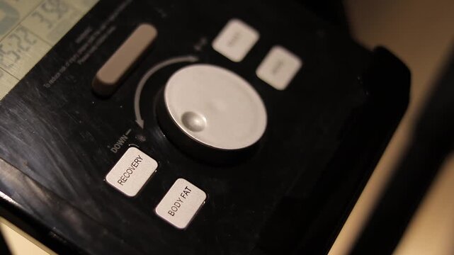 A person's hand is shown adjusting the controls of a modern exercise machine's console, featuring a digital display and various buttons.