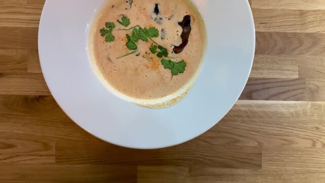 Creamy mushroom puree soup white plate on wooden table restaurant closeup, garnished with herbs and mushroom slice, warm natural