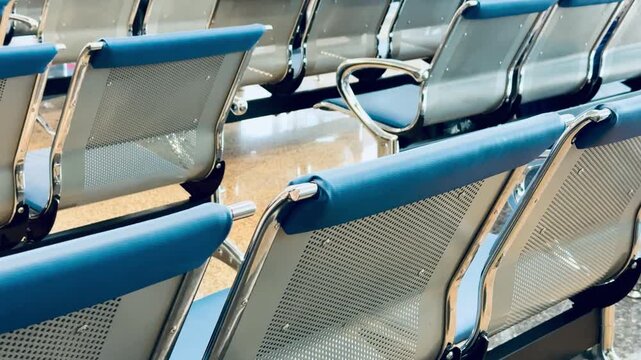 Empty metal benches at railway station, rows of blue cushioned perforated seats with chrome frames reflecting light on polished