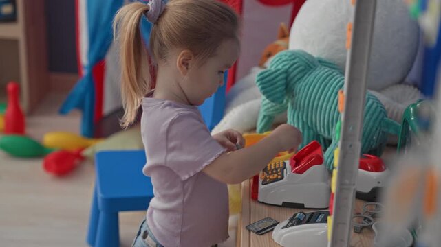 Girl adjusts round toy glasses while pressing buttons on a toy cash register in a playroom building; concentration imagination.