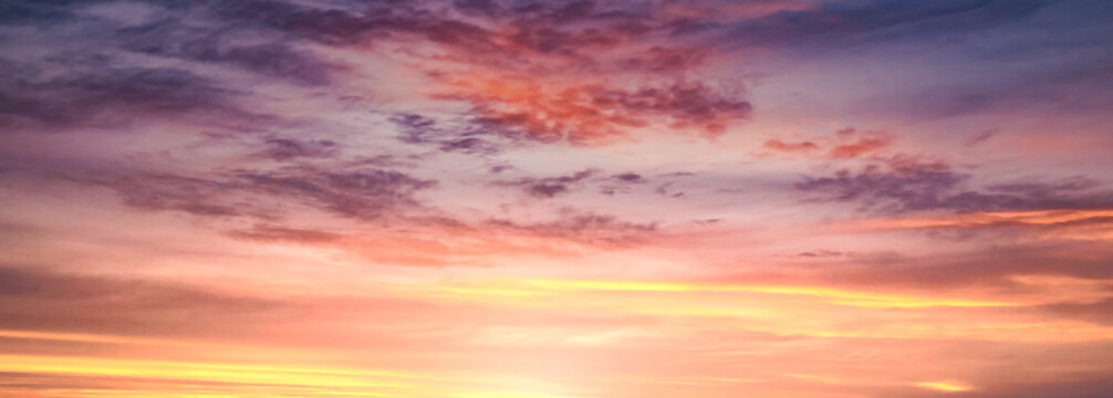 Beautiful dramatic twilight sky background with colorful pastel pink purple and golden orange clouds at sunset for inspirational nature wallpaper panorama