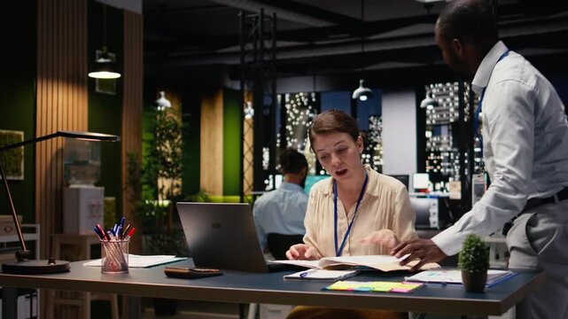 Group of colleagues engaged in teamwork during late night briefing session, using reports and documents to forecast business outcomes and set goals. Refining strategy and action plan.
