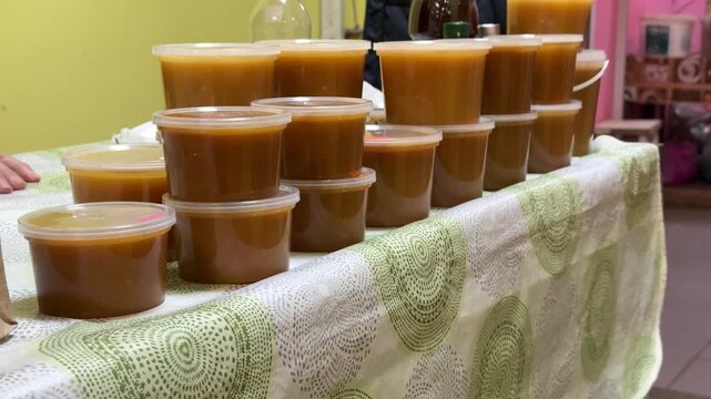 Close-up honey jars on counter warm amber honey in clear plastic containers stacked on cloth market display glossy texture visible