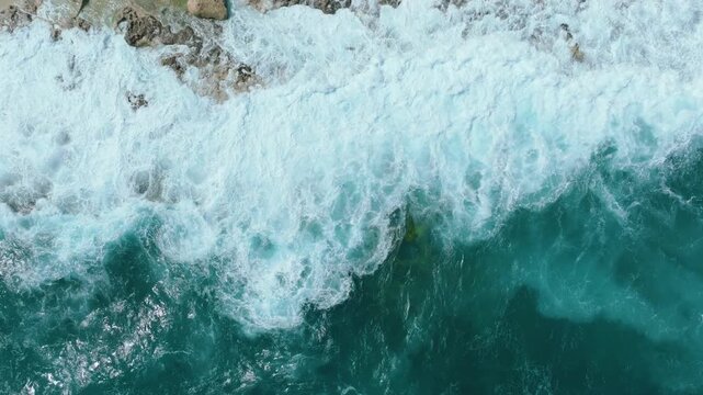 Top down drone view of ocean waves crashing on rocky coastline in Malta with sea foam and textured shoreline in slow motion Powerful waves roll toward a rocky shoreline and break against the coast