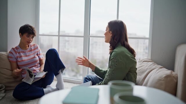Two happy readers discussing literature sitting home floor. Two women talking