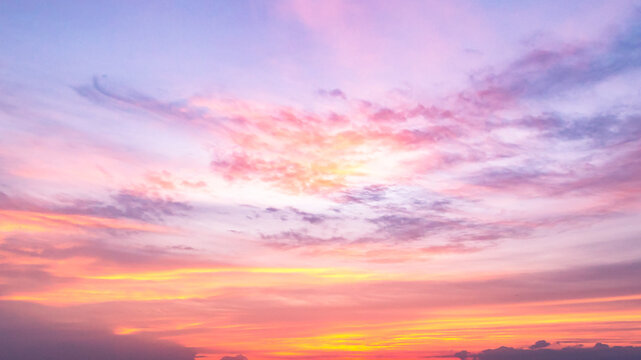 Beautiful vibrant twilight sky background with colorful pastel pink purple and golden orange clouds at sunset for inspirational nature wallpaper