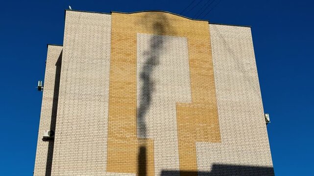 Shadow gas pipe smoke on brick facade under clear blue sky, sunlight casts dark silhouette and elongated pipe shadow
