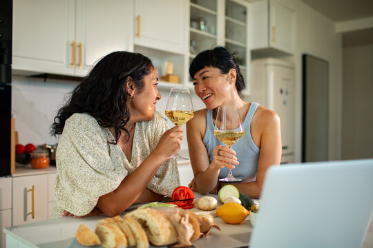 Two women toasting wine while cooking in a home kitchen