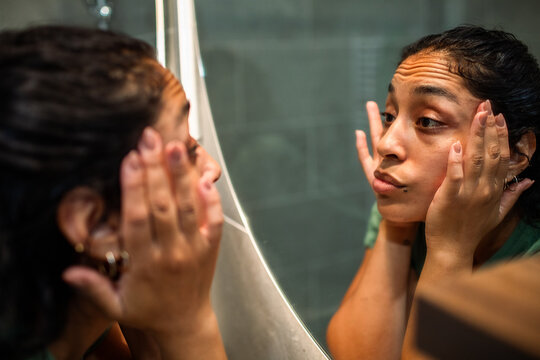 Woman examining her face in a bathroom mirror