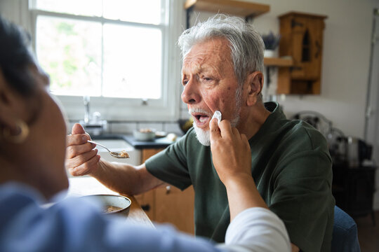 Caregiver feeding senior man in home kitchen