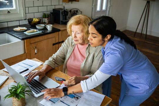 Caregiver helping senior pay bills online at home kitchen