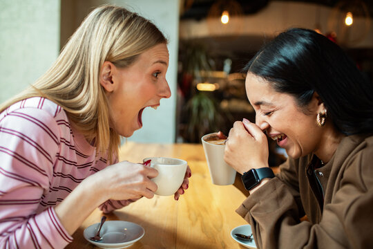 Two friends laughing over coffee at a cozy cafe